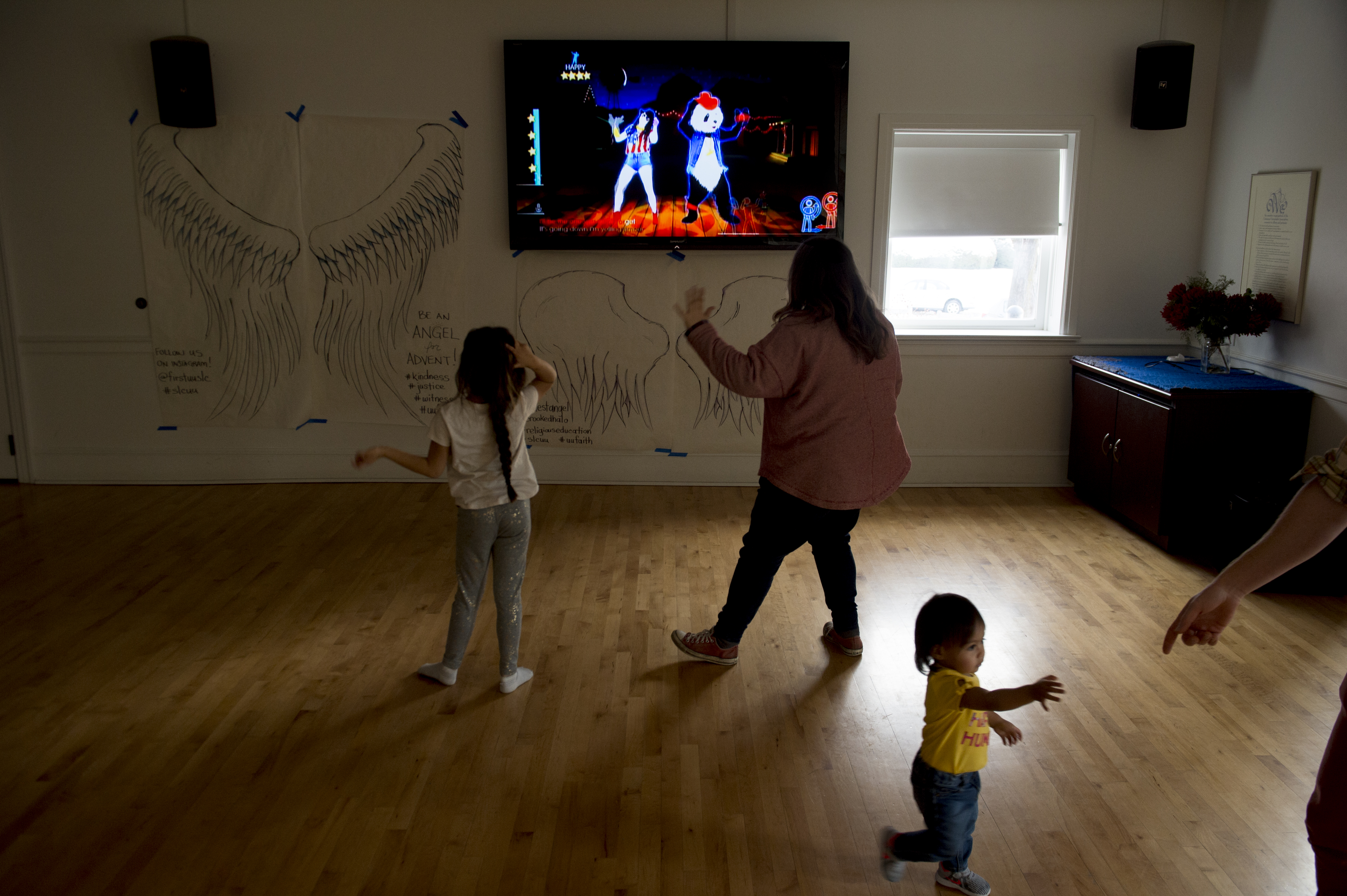 (Jeremy Harmon | The Salt Lake Tribune) Seven-year-old Yaretzi plays a dance game with volunteer Tiffany Young at the First Unitarian Church on 1300 East in Salt Lake City on Dec. 14, 2018. Seventeen-month old Bella reaches for the hand of volunteer Easton Smith so she can join in the game.