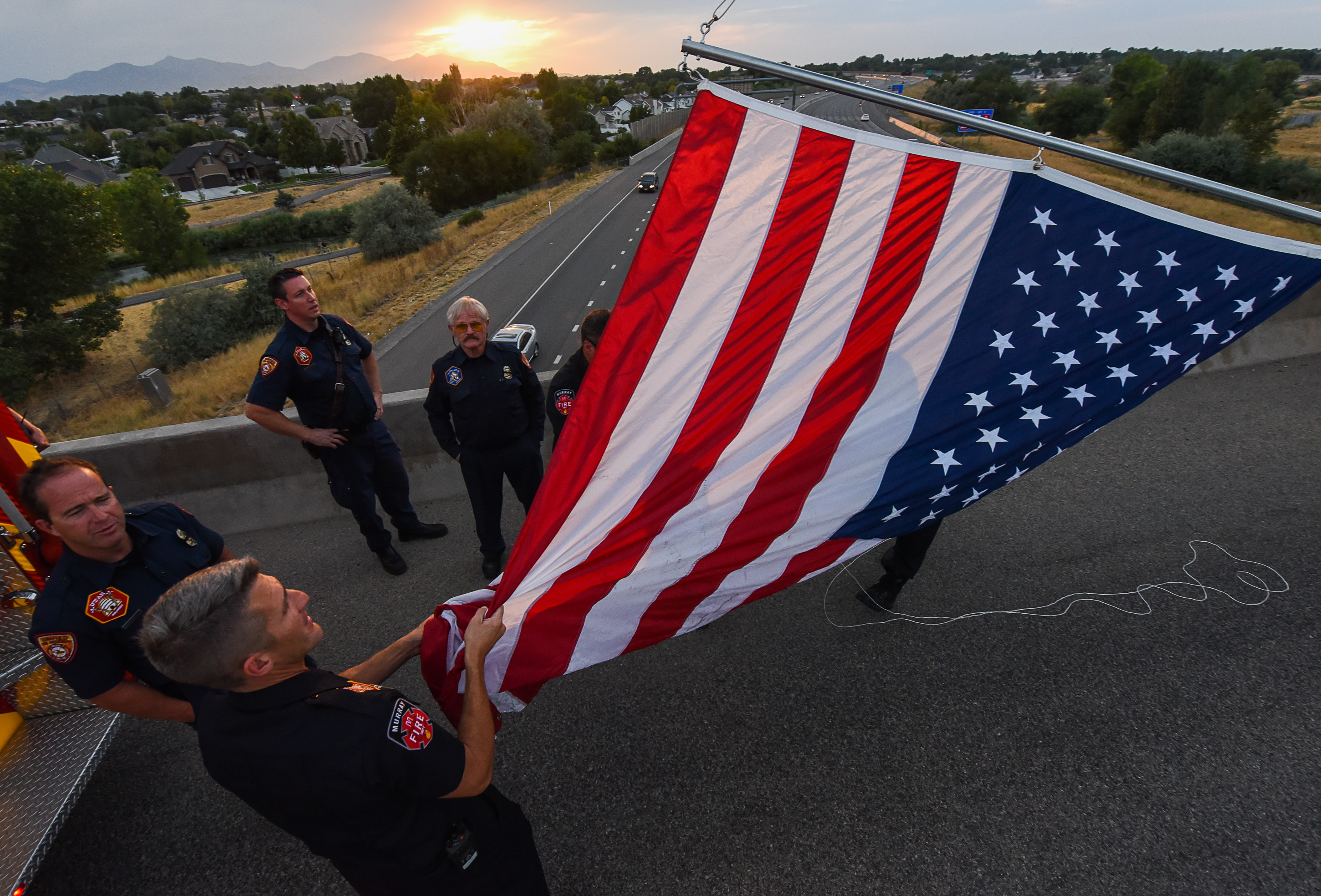 (Francisco Kjolseth | The Salt Lake Tribune) Firefighters unfurl a flag as they get ready to honor Utah firefighter Matt Burchett, 42, who died fighting a wildfire in California. His body was being returned home, to travel along I-215 after being flown in to the Utah Air National Guard in Salt Lake City on Wed. Aug. 15, 2018. The remains of the Draper battalion chief were transported to Jenkins-Soffe Mortuary in South Jordan.