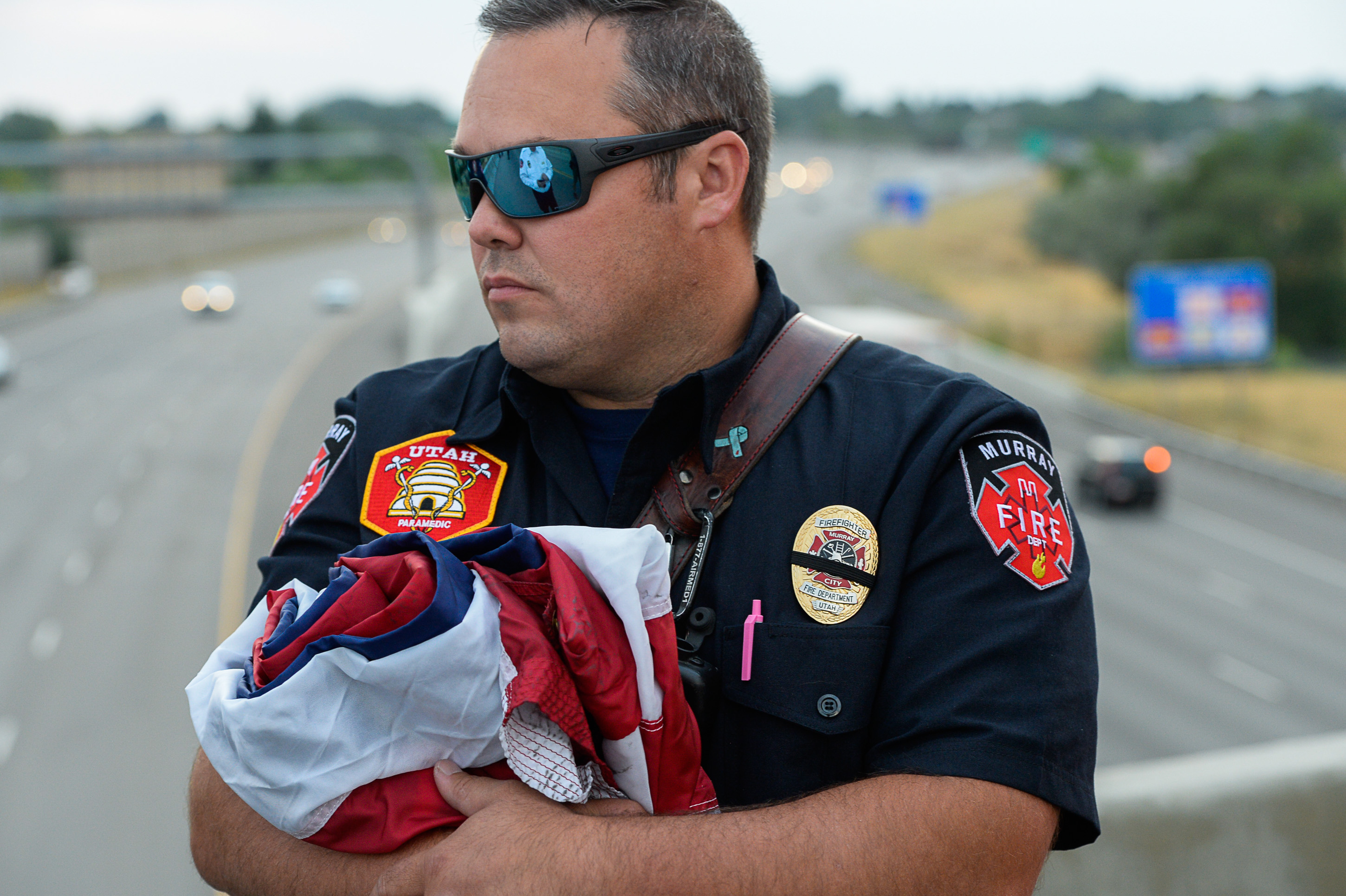 (Francisco Kjolseth | The Salt Lake Tribune) Jason Hawkes with Murray Fire Tower 83, holds a flag to be unfurled over I-215 in Murray in anticipation of the arrival of the body of Utah firefighter Matt Burchett, 42, who died fighting a wildfire in California. Several firefighter details set up along the procession route after being flown in to the Utah Air National Guard in Salt Lake City on Wed. Aug. 15, 2018. The remains of the Draper battalion chief were transported to Jenkins-Soffe Mortuary in South Jordan.