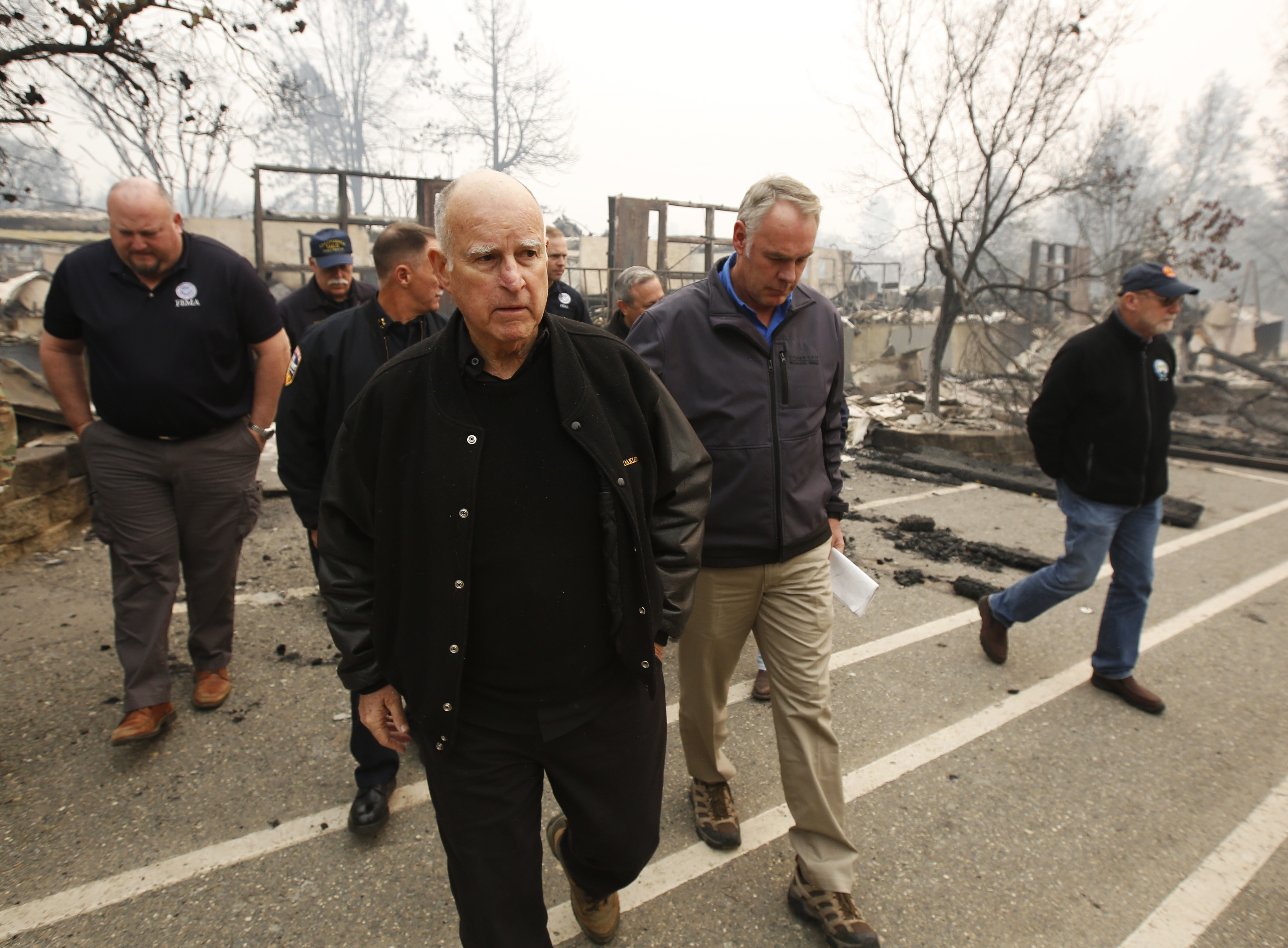 California Gov. Jerry Brown, center, and Interior Secretary Ryan Zinke, second from right, tour the fire ravaged Paradise Elementary School Wednesday, Nov. 14, 2018, in Paradise, Calif. The school is among the thousands of homes and businesses destroyed along with dozens of lives lost when the fire burned through the area last week. (AP Photo/Rich Pedroncelli)