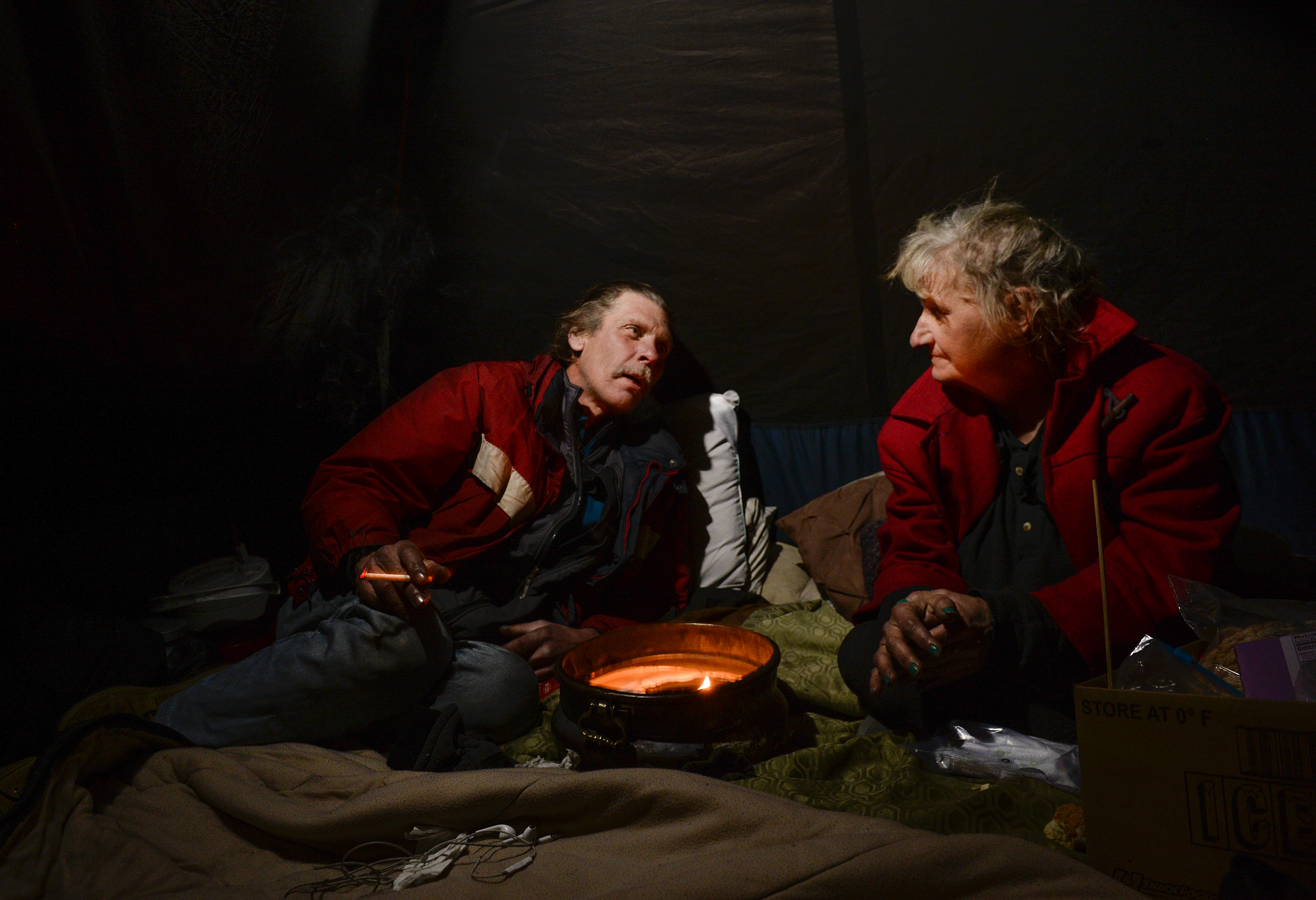 (Leah Hogsten | The Salt Lake Tribune) Ron Barrett, 55, and his wife Katherine Barrett, 54, who are homeless try to stay warm in their tent from the meager heat from a ceramic pot filled with candle wax. Their cold hands are blacken by the soot rising from the burning candle on a night that temperatures dropped to 12 degrees in Salt Lake City. "It's crazy, you gotta be able to have a sense of humor," said Ron Barrett, 55, of the life circumstances that resulted in life on the streets for he and Katherine since 2017. The Barretts are trying to find housing through a Shelter Plus Care housing voucher through the Salt Lake City Housing Authority. The couple says they refuse to stay in the state's largest homeless shelter, The Road Home on Rio Grande Street, because of past threats of violence from other residents.