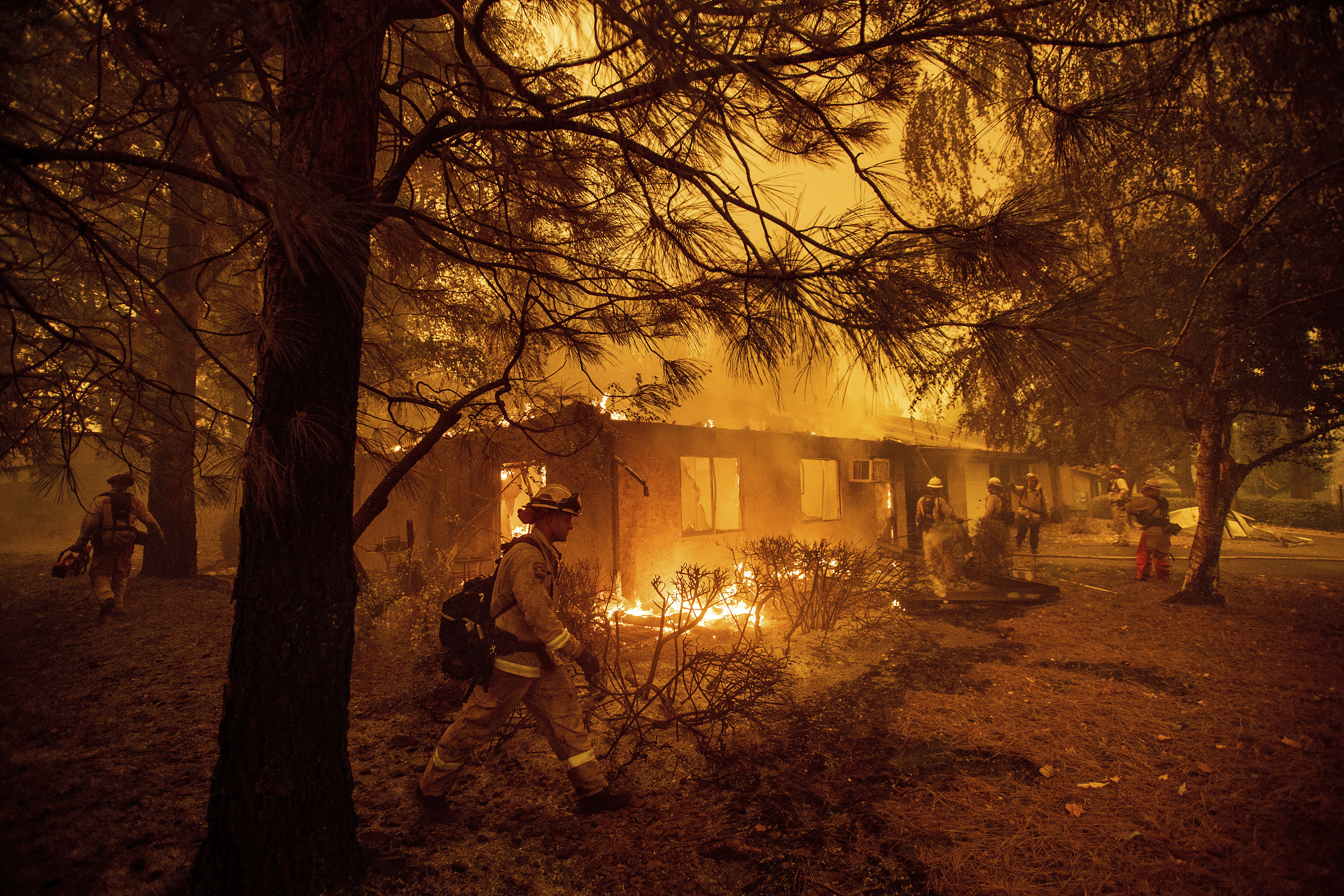 FILE- In this Friday, Nov. 9, 2018, file photo firefighters work to keep flames from spreading through the Shadowbrook apartment complex as a wildfire burns through Paradise, Calif. California wildfires have been so frequent that the state government recently passed a spate of laws intended to help victims of wildfires, but experts say it can still sometimes take years for a home to be rebuilt. (AP Photo/Noah Berger, File)