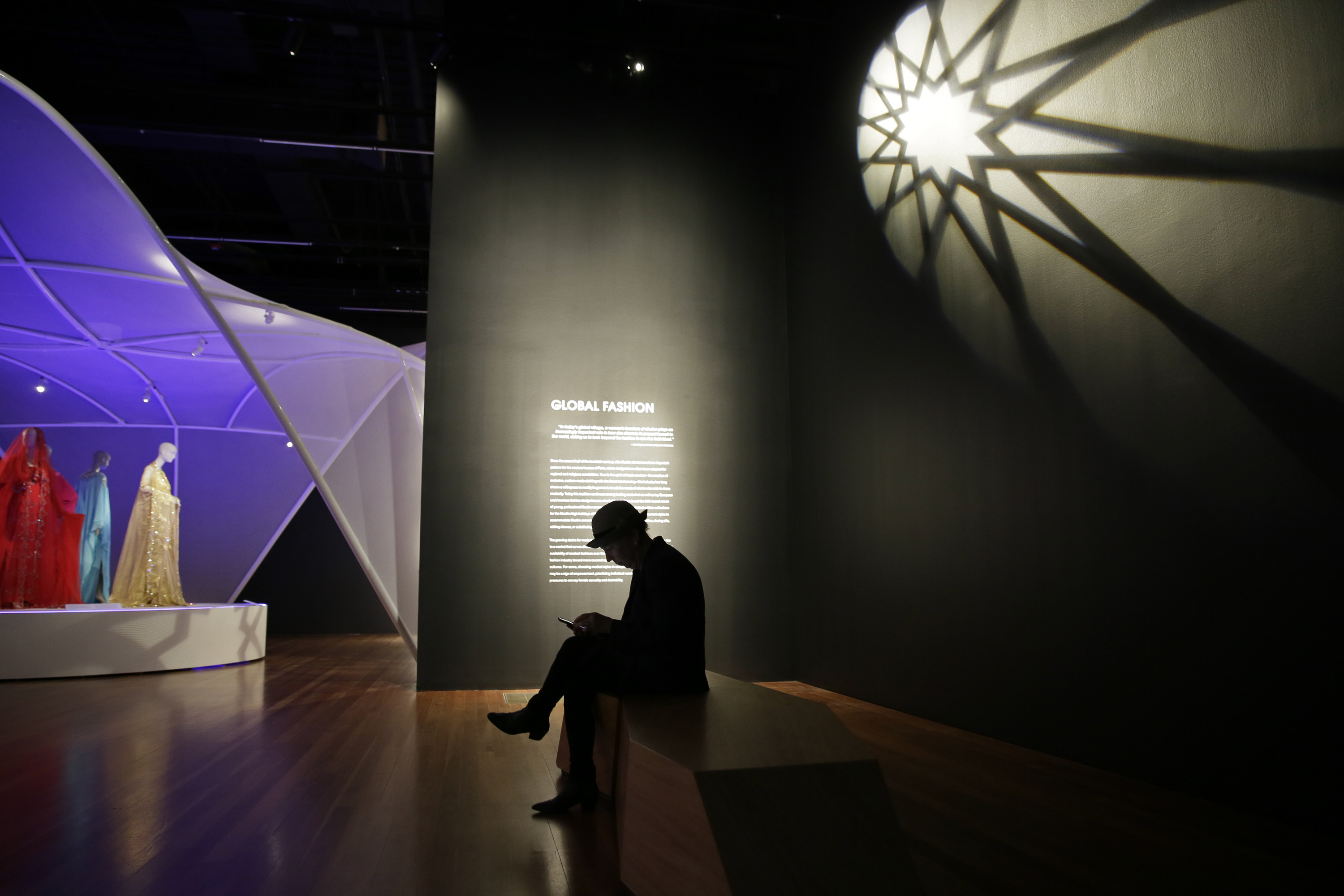 (Eric Risberg | AP Photo) In this photo taken Thursday, Sept. 20, 2018, a man sits in a section on global fashions in the exhibit Contemporary Muslim Fashions at the M. H. de Young Memorial Museum in San Francisco. The first major museum exhibition of contemporary Muslim women's fashion reflects designs from around the world that are vibrant and elegant, playful and diverse. The show's creators hope the exhibit will show Muslim women as real people who can choose what they wear rather than as subjects ordered to cover their entire bodies or restricted in what they can wear. The exhibit opens on Saturday.